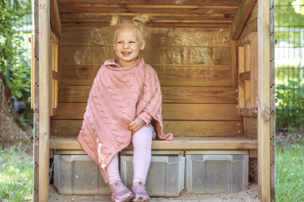Blondes Mädchen mit rosa Poncho, Kindergartenfotografie im freien Spiel Berlin