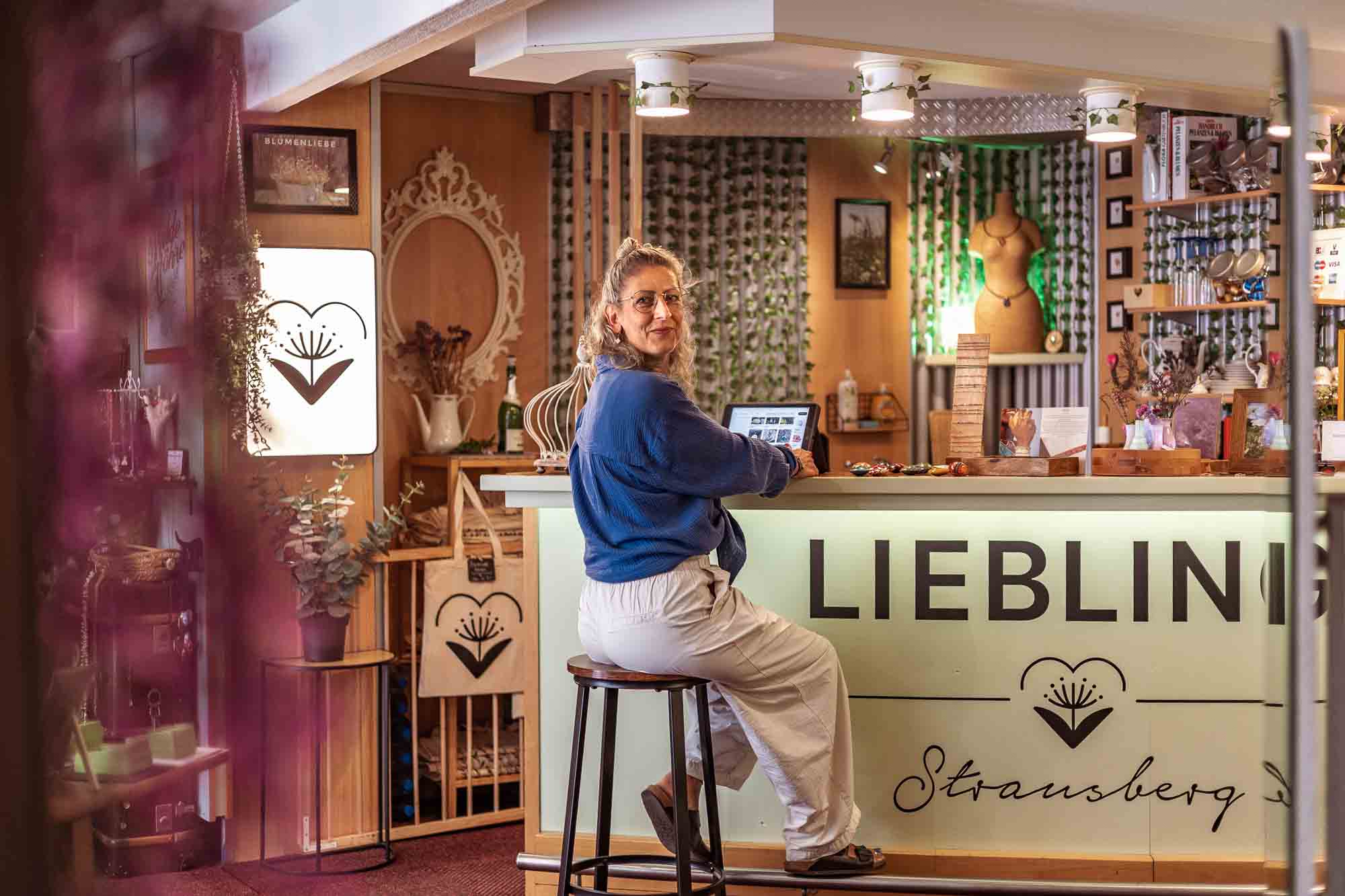 Authentische Businessfotografie Strausberg: Ladenbesitzerin im Schmuckgeschäft Liebling am beleuchteten Tresen mit Logo, handgemachter Schmuck aus Blüten und Blättern, Branding für kreative Unternehmerinnen.