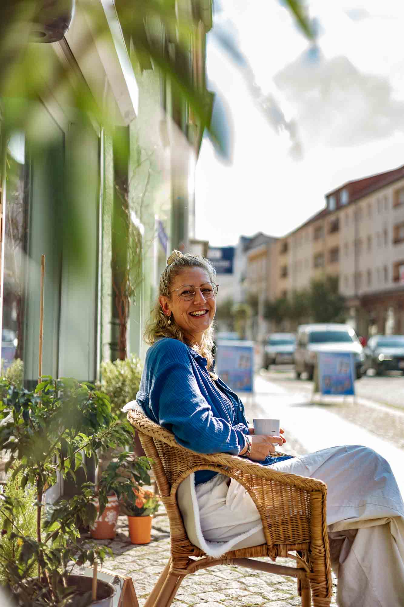 Echte Unternehmerinnen-Portraits – JessyGraphy Unternehmensfotografie Inhaberin von Liebling Strausberg sitzt entspannt vor ihrem Laden in der Sonne – authentische Businessfotografie in Brandenburg