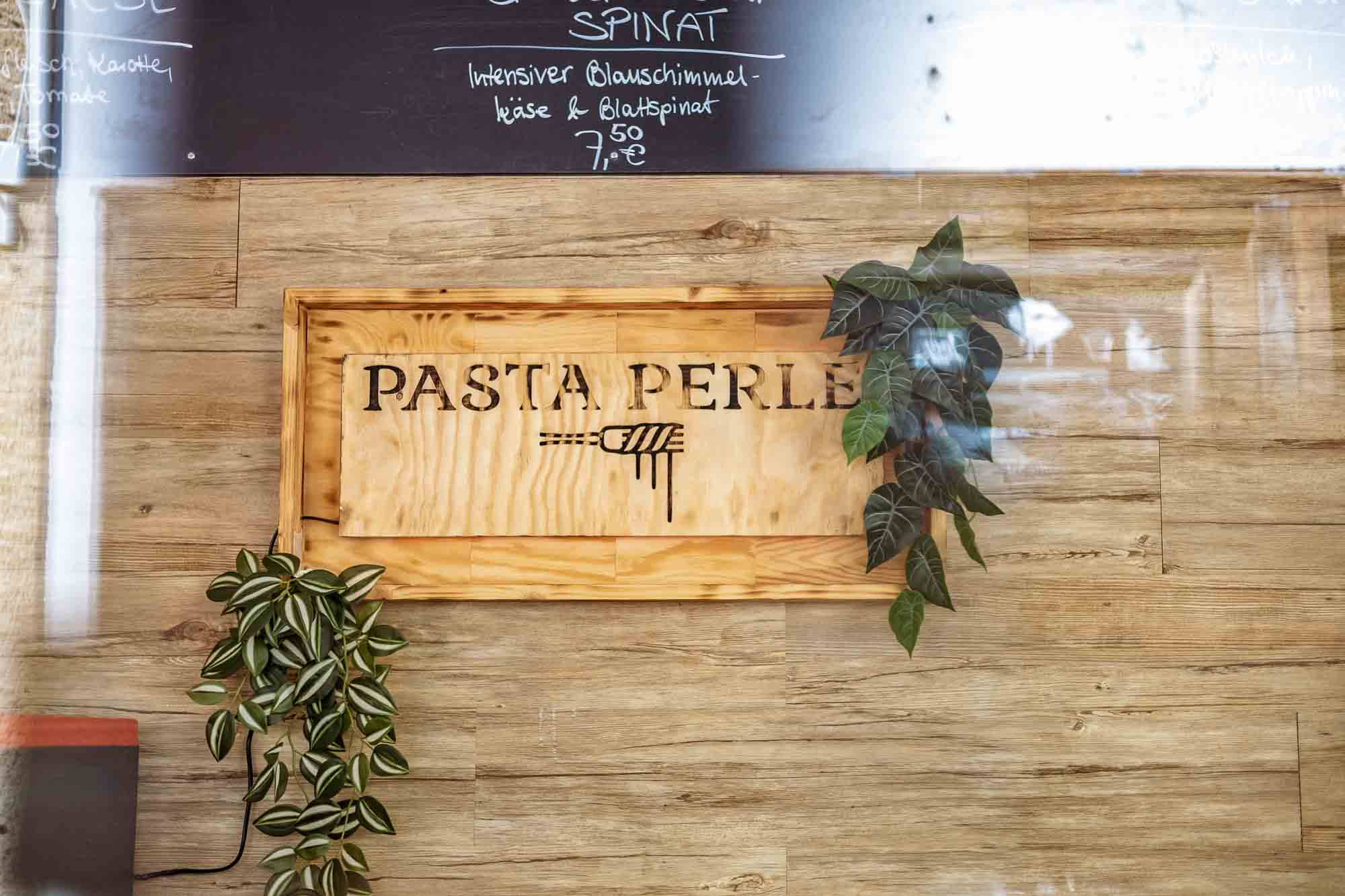Businessfotografie Gastronomie: Restaurant-Schild Pasta Perle in Berlin mit Pflanzen und Holzdekor, authentische Imagefotos für Unternehmen, Markenauftritt, Food- und Gastrofotografie mit natürlichem Look.