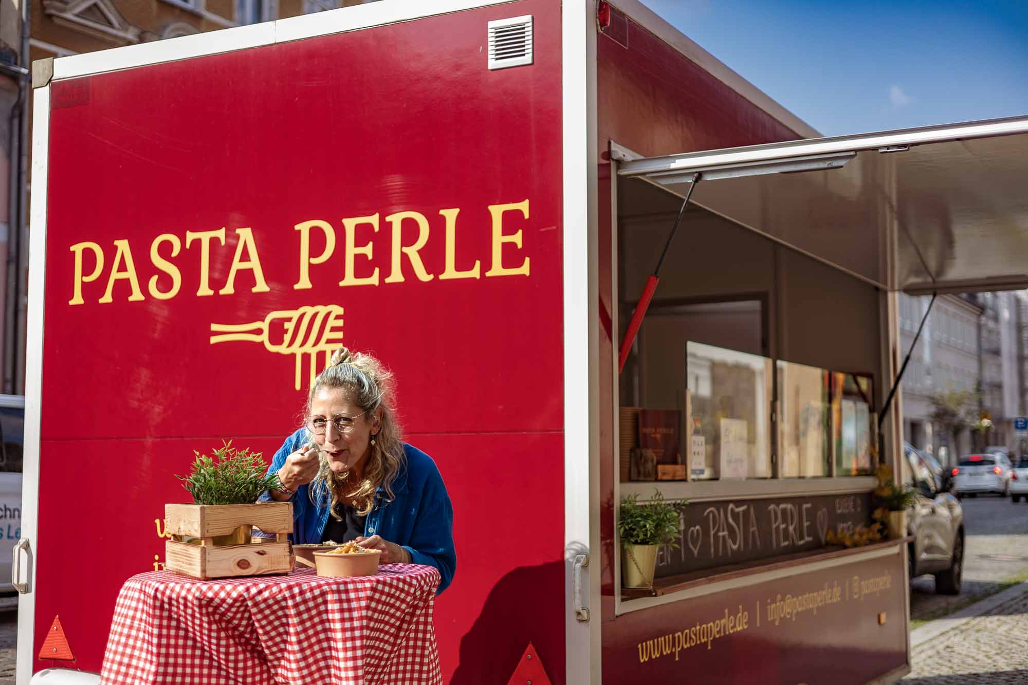 Pasta Perle Foodtruck Berlin, Kundin genießt frische Pasta am rot-weiß gedeckten Tisch, authentische Businessfotografie Gastronomie, Streetfood Branding und mobile Küche.