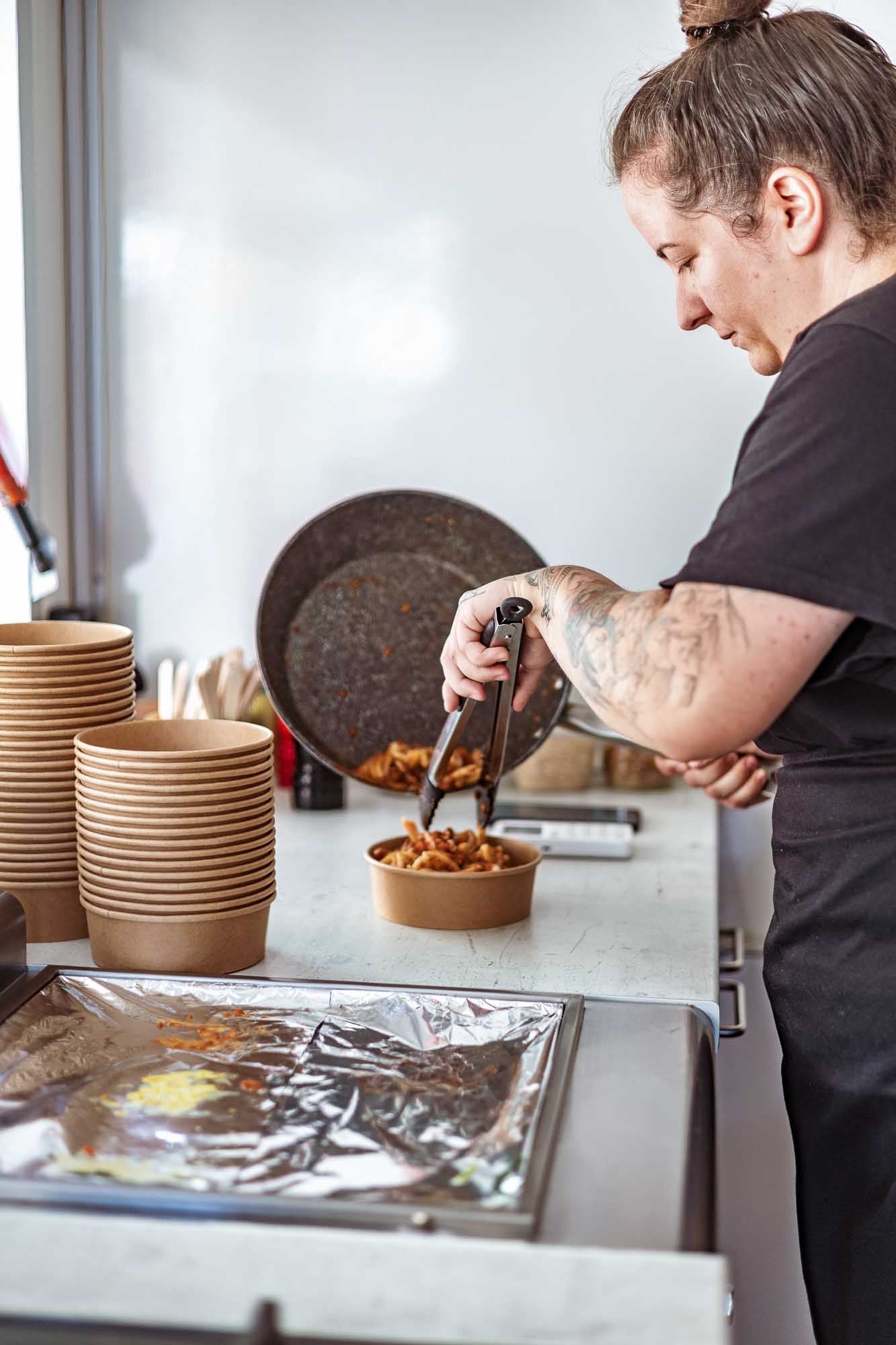 Foodfotografie und Business Branding: Köchin Anne bereitet Pasta in Pfanne auf Gasherd zu, authentische Küchenaufnahme für Foodtruck und Gastronomie in Berlin.